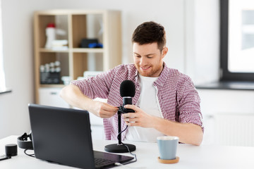 technology, podcast and people concept - male audio blogger with laptop computer connecting cable to microphone at home office