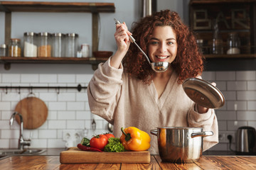 Photo of kind caucasian woman holding cooking ladle spoon while eating soup at home