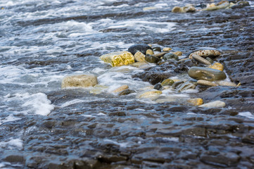 pebble stones on the sea beach, the rolling waves of the sea with foam