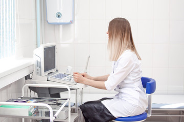 Blonde woman doctor in white uniform in clinic hospital works on ultrasound scanner. Diagnostics, sonography and health concept. copyspase