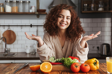 Photo of pretty caucasian woman smiling while cooking salad with fresh vegetables at home