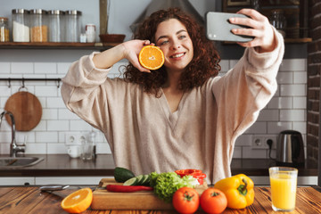 Image of adorable caucasian woman taking selfie photo on smartphone while cooking at home