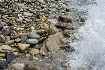 pebble stones on the sea beach, the rolling waves of the sea with foam