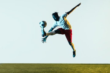 Fototapeta na wymiar Young african-american male football or soccer player in sportwear and boots kicking ball for the goal in neon light isolated on white background. Concept of healthy lifestyle, professional sport