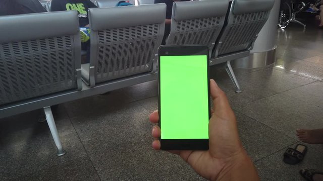Close up hand holding using mobile smart phone green screen in community mall, shopping center. Royalty high quality free stock video footage of holding a smartphone green screen display in the hand