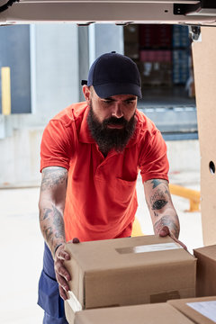 Serious worker putting package into the car.