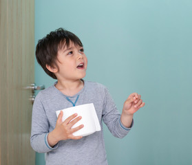 Portrait of cute boy holding toilet roll standing in front of toilet, Child with smiling face carrying toilet roll and looking up, Children health care concept