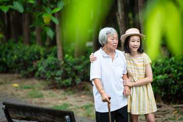 Asian little girl supporting senior woman with walking stick,happy smiling grandmother and granddaughter in the park,elderly people walking exercise for health,concept family;summer and vacation