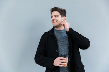 Image of european young man holding takeaway coffee while standing isolated over gray wall background