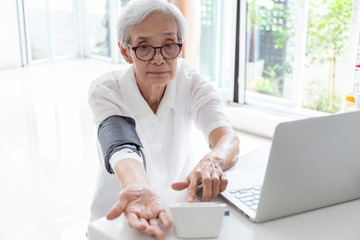 Senior woman checking blood pressure with device and laptop