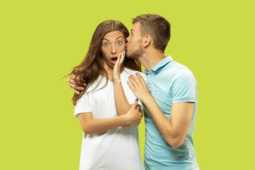 Beautiful young couple's half-length portrait isolated on green studio background. Woman and man standing, caddling and kissing . Facial expression, human emotions concept. Trendy colors.