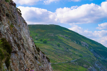 Rolling green hills and cliff face in Wicklow, Ireland with blue sky and white fluffy clouds in summer.