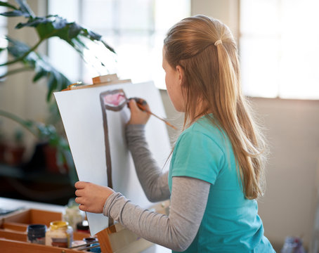 Creative young girl painting on easel