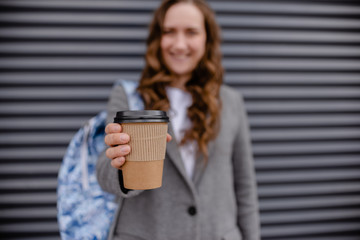 Young woman with beverage laughing near wall