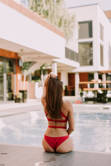 Attractive young woman in red bikini sits by the poolside and enjoys the summer sun