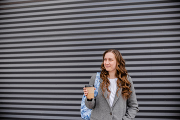 Young woman with beverage laughing near wall