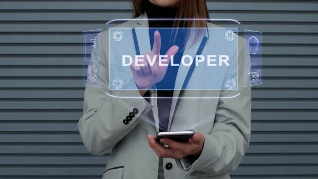 Unrecognizable business woman, interacts with a HUD hologram with text Developer. Girl in a business suit uses the technology of the future mobile screen against the background of a striped wall