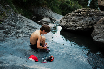little boy getting undressed about to swim in a stream