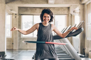 Poster Beautiful young smiling happy Caucasian sporty woman with short hair playing hula hoop inside gym studio with treadmills behind - fun workout fitness portrait concept © twinsterphoto