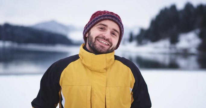 Happy tourist are getting freezing outside , standing closeup of the camera background big lake and snowy forest and mountain, he shows a big like in front of the camera