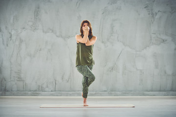 Full length of beautiful Caucasian brunette standing on the mat barefoot in Eagle yoga pose.