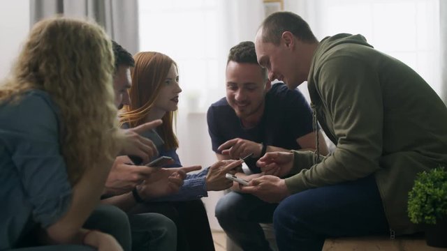 Happy friends group using phones sit on sofa indoor laughing talking having fun