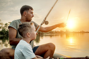 Happy Father and Son together fishing from a boat at sunset time