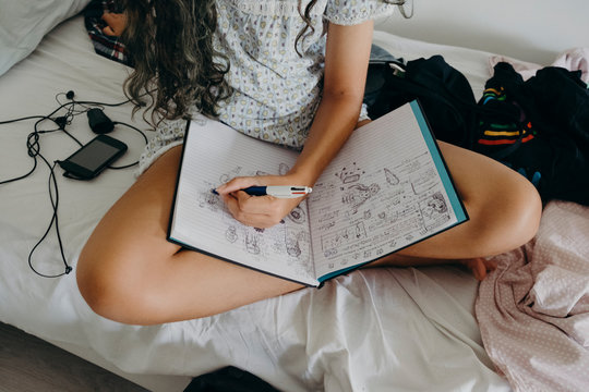 Anonymous young female model woke up and drawing in her sketch book in bed