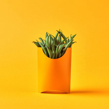 Yellow paper lunch box with organic raw French beans on a yellow