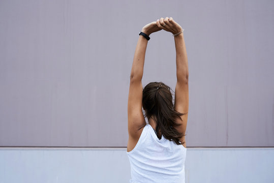 Minimal view of sportswoman stretching arms against wall.