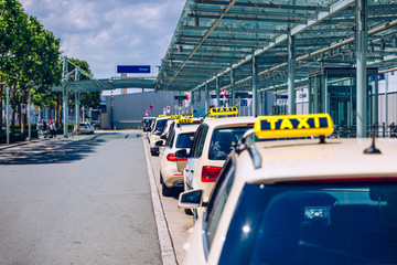 Taxi cabs waiting for passengers. Yellow taxi sign on cab cars. Taxi cars waiting arrival passengers in front of Airport Gate. Taxis stand on Airport Terminal waiting for passengers.