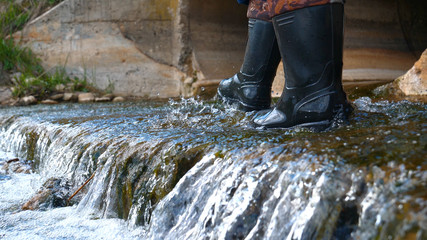 A worker in a working uniform, rubber boots checks the sewage canal inside it and write down on...