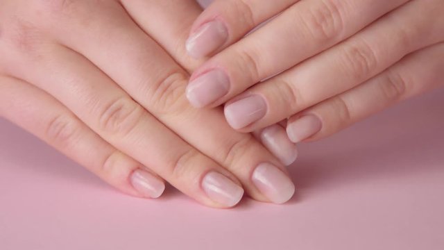 closeup woman hand on pink and other hand tpuches another.Ideal natural manicure