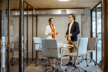 Young man and woman having a business conversation during the small conference, standing near the table in the meeting room