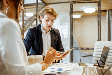 Young man and woman having a serious business conversation, working with paper documents and computer in the office