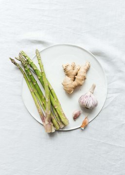 Still life of asparagus, ginger, garlic on ceramic plate with linen tablecloth