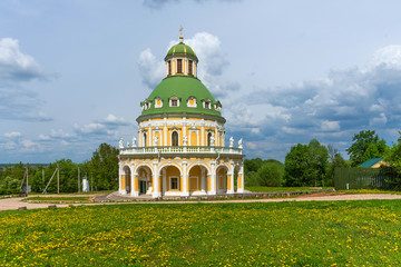 Fototapeta na wymiar Church of the Nativity of the Virgin in Podmoklovo, Russia. Spring day with a dramatic sky. Flowering dandelions.