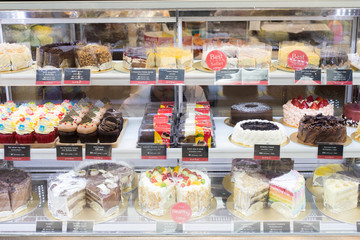 Many Good Looking design and colorful Bakery Cake in refrigerator windows show, present variety of Price and vanilla chocolate birthday cake for special occasion, blur by frozen ice glass