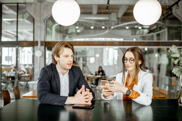Young man and woman having business conversation while sitting together in the bar or coworking space