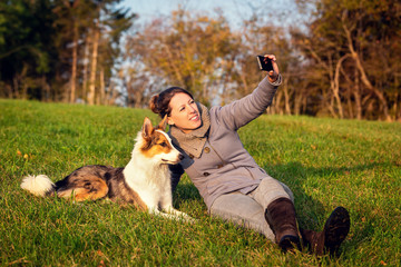 Frau liegt auf einer Wiese und macht einen Selfie mit ihrem Hund