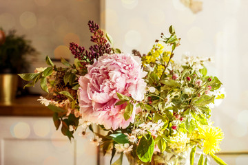 A spring bouquet of pink peony flowers, a blossoming apple tree branch, a lilac flower and wild flowers in a transparent jug are in the kitchen. Copy space.