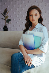 Portrait of attractive young female doctor sitting on the sofa in the office with notebook, book, folder and smiling. Medical concept. Healthcare