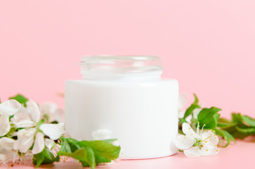 Fototapeta na wymiar Face cream in white jar on a pink background with white flowers. Concept natural cosmetics, organic beauty. Copy space.