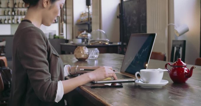 Woman using laptop with tea cup.Back view.Casual dressed asian chinese,caucasian women working business or studying at pub cafe,restaurant lounge or cafeteria.Modern,coworking,diversity,multiethnic