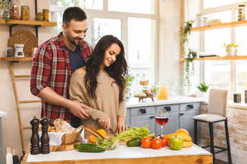 Beautiful young smiling happy couple is talking and smiling while cooking healthy food in kitchen at home.