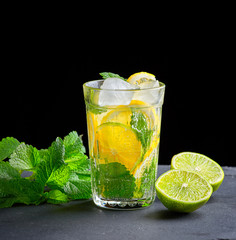 cold drink made from pieces of lemon, lime and leaves of green mint in a glass with water drops