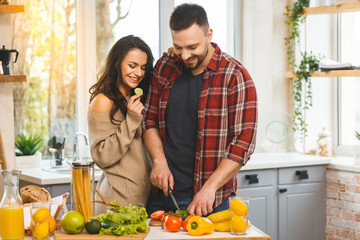 Beautiful young smiling happy couple is talking and smiling while cooking healthy food in kitchen at home.