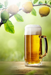 Fresh cold beer on wooden table. Branch of fresh lemons fruits and summer garden background 