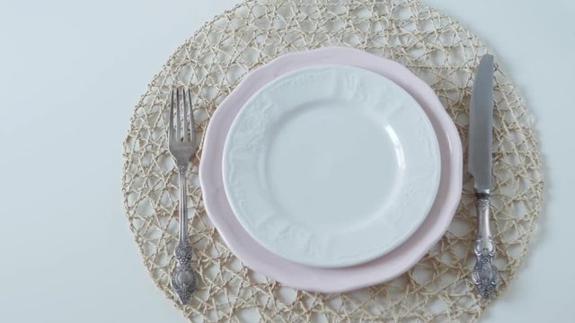 table setting with white dishes on white background. boiled egg for breakfast. female hands lay an egg in a plate.