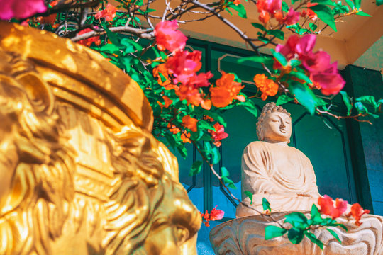 Stone carved statue of Buddha surrounded with colorful flowers